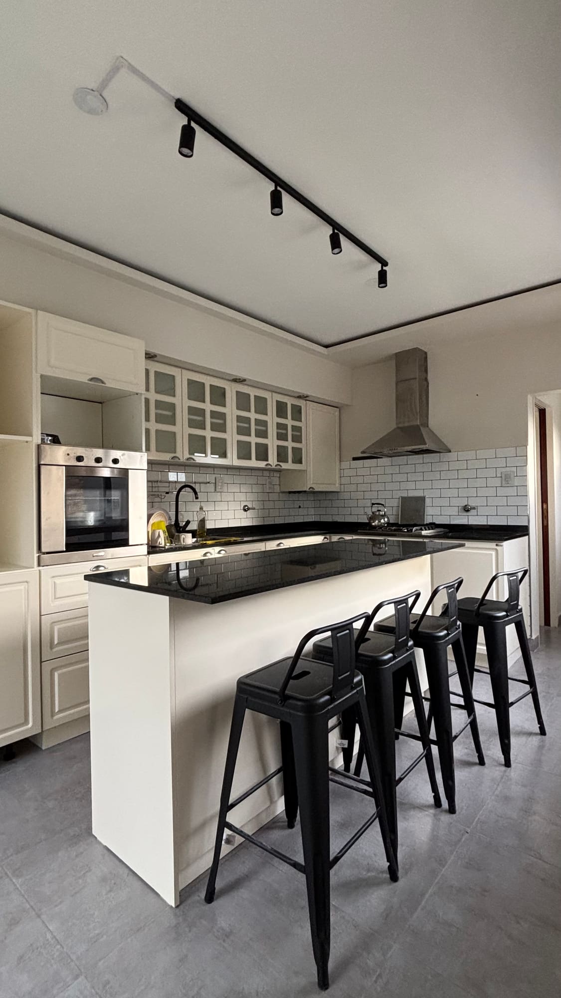 Cocina con isla central, banquetas negras y equipamiento blanco